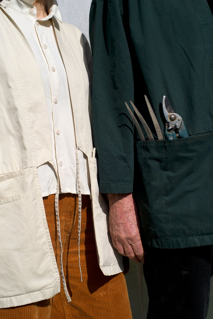 Elderly couple wearing a heavy organic cotton drill garden kimono, the man in the colour Laurel Green showing the unique features of the large pockets in front of the Kimono and the women in the colour Sandstone. 