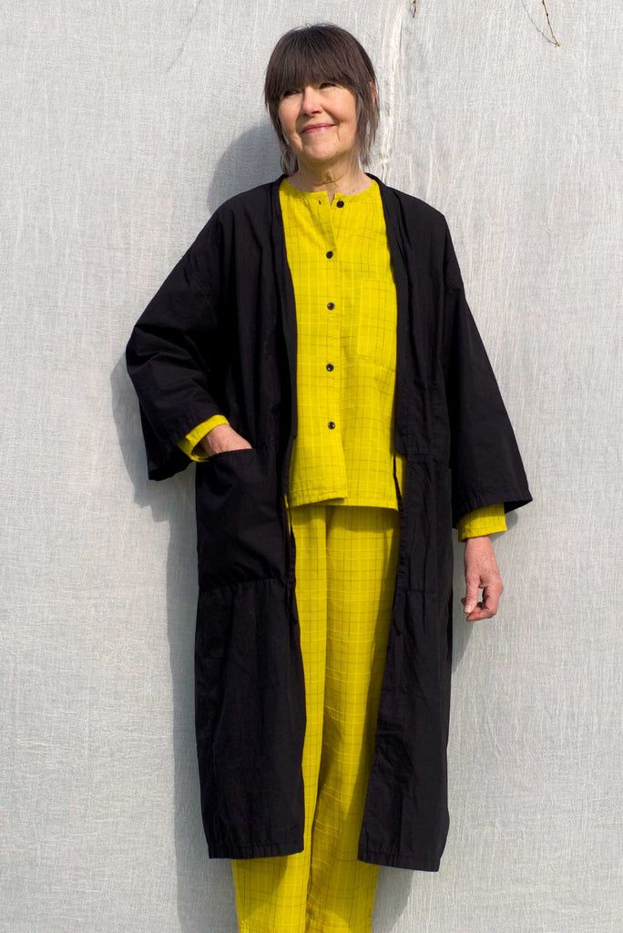An elderly lady wearing a lightweight organic cotton house kimono in the colour dexter black whilst posing with one of her hands in the deep front pocket.